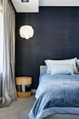 Double bed in front of shimmery, midnight blue, fabric wallpaper