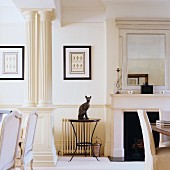 Animal ornament on round side table between open fireplace and classical columns in traditional, white living room
