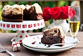 Schokoladen-Haselnuss-Kuchen mit Baiserhaube auf Kuchenständer und Teller, rote Rosen in einer Vase