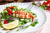 A salmon fillet on a bed of lamb's lettuce with tomatoes, avocado and pesto