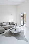 Puristisches Wohnzimmer in Grau/Weiß mit Designertisch auf Tierfell und Überecksofa