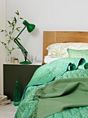 Bed with a wooden headboard and plaid pattern next to a night stand with a green, retro table lamp