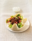 A tortilla bowl filled with lettuce, minced meat and tomatoes