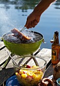 Barbecued pork belly with potato salad on a wooden jetty by a lake