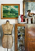 Crystal glasses in vintage, glass-fronted cabinet next to antique tailor's dummy