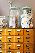 Gifts in large glass jars with lids on antique apothecary cabinet with alphabetically labelled drawers