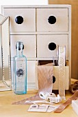 Small chest of drawers full of ribbons behind bluish vintage bottle