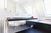 A designer bath under the roof and a generous washbasin over a cupboard with a shiny metal front