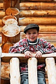 Young boy leaning on a wooden railing in front of a log cabin