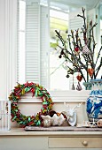 Advent wreath wrapped with colourful ribbons and Christmas tree decorations on branches in ceramic vase