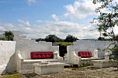 Whitewashed masonry benches and tables with red seating cushions in front of open landscape