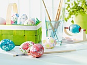 Painted Easter eggs in front of basket of eggs and paintbrushes in glass of water