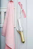Rosa Handtuch und Retro Lockenstab auf Haken an weiße Holzwand gehängt