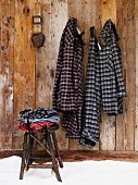 Clothing on rustic stool next to checked pyjamas hanging from pegs on wooden wall