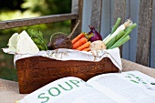 Fresh vegetables from the garden in a wooden crate, and an open cookbook
