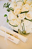 White bridal bouquet behind scrolls of paper bearing names of bride and groom