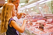 A mother and daughter at the meat counter in a supermarket