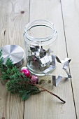 Star-shaped cookie cutter in a screw top jar, next to it a pine branch and Christmas ornaments