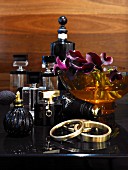 Various elegant perfume bottles, bowl of orchid flowers and bracelets on black dressing table