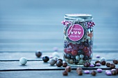 Verschiedene Süssigkeiten (Jelly Beans, Lakritze- und Schokodragees) in einem Einmachglas als Geschenk