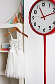 White tulle dress on wooden clothes hanger and red station clock in girl's bedroom
