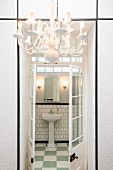 Blick durch geöffnete Sprossenflügeltür ins Badezimmer mit Säulenwaschbecken; weiß tapezierter Einbauschrank und Kronleuchter im Vordergrund