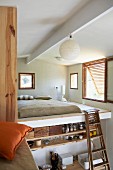 View of sleeping area in mezzanine with wooden ladder above simple kitchen