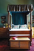 Wooden bed with ruched canopy flanked by bedside cabinets with drawers and with trunk at foot