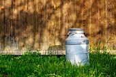A milk churn in the grass outside a wooden cabin