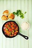 Spicy turkey goulash in the pan with rice and bread rolls