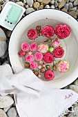 Roses floating in enamel bowl arranged with white linen towel and soap dish on gravel floor