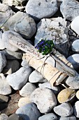 Lovingly wrapped gift decorated with driftwood and forget-me-nots on pebbly beach