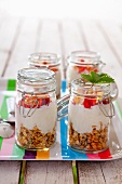 Four jars containing ingredients for muesli: rolled oats, vanilla yoghurt and strawberries