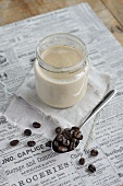 Milchkaffee in einem Schraubglas, daneben Kaffeebohnen