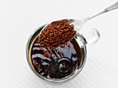 Instantkaffeepulver wird mit Löffel in Glastasse gegeben