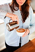 Frau gießt Milchschaum in Kaffeetasse