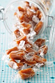 Karamellbonbons in Einwickelpapier fallen aus Glasgefäss