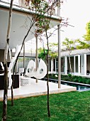 White chair hanging from roof of veranda alongside pool in courtyard of contemporary house