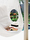 Sunhat and book in white, wicker hanging chair with cushions