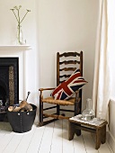 Union Jack pillow on an old rocking chair, wooden stool and basket with firewood by a fireplace