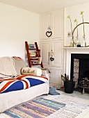 Sofa with Union Jack seat cushions and wooden ladder with books next to a white built-in cupboard