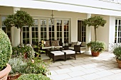 Braune Outdoormöbel auf Steinboden einer Terrasse mit Säulen und Fenstertürfront einer traditionellen herrschaftlichen Villa
