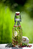 Kräuteröl in einer Flasche auf Holzbrett im Garten