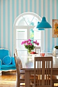 Dining table with wooden chairs and blue upholstered armchair in front of an arched window