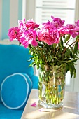 Peonies in a vase on a wooden table in front of an armchair