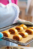 A woman holding a baking tray of freshly baked yeast dumplings with a lentil and tomato filling