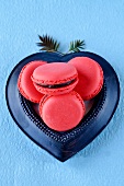 Raspberry macaroons with chocolate filling in a heart-shaped dish on a blue surface