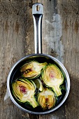 Halved purple artichokes in a saucepan of water on a rustic wooden surface