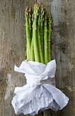 Stalks of green asparagus wrapped in white paper on a wooden surface