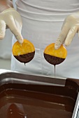 A chocolatier dipping candied orange slices into melted chocolate